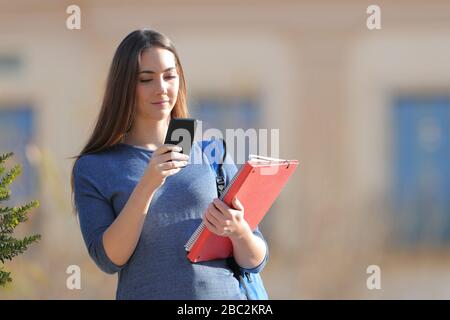 Serio studente in piedi in possesso di cartelle di controllo smartphone in un campus una giornata di sole Foto Stock