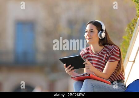 Studente con cuffie e tablet elearning che guarda lontano seduto in un campus Foto Stock