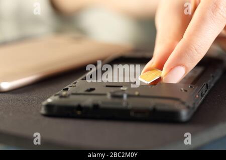 Primo piano delle mani della donna inserimento della scheda sim sullo smartphone su una scrivania Foto Stock