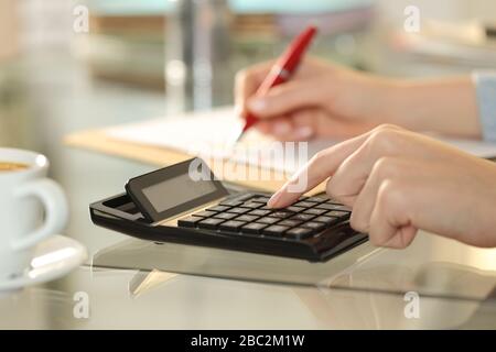 Primo piano delle mani della donna utilizzando la calcolatrice e scrivendo su un documento su una scrivania a casa Foto Stock