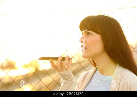 Donna adulta che parla registrare il messaggio utilizzando il riconoscimento vocale sul telefono cellulare in strada al tramonto Foto Stock