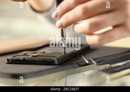 Primo piano delle mani della donna rimozione delle viti su uno smartphone su una scrivania Foto Stock