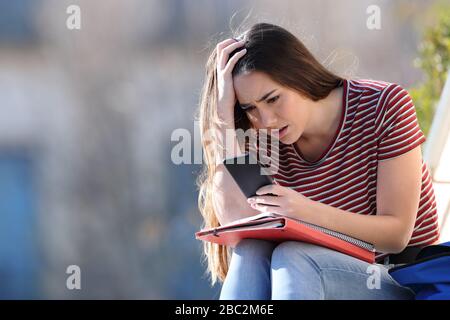 Gli studenti preoccupati di controllare le cattive notizie sul telefono cellulare seduto in un campus Foto Stock