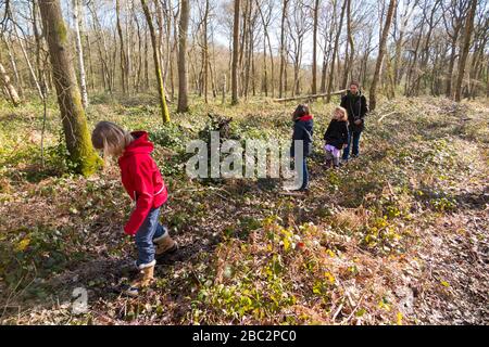 Figlia madre leader di 3 bambini tre figlie bambini a piedi / camminare lungo il sentiero frondoso e fangoso / nel fango su bosco passerella percorso pedonale sentiero. West End Common, vicino a Esher nel Surrey, Regno Unito. (116) Foto Stock