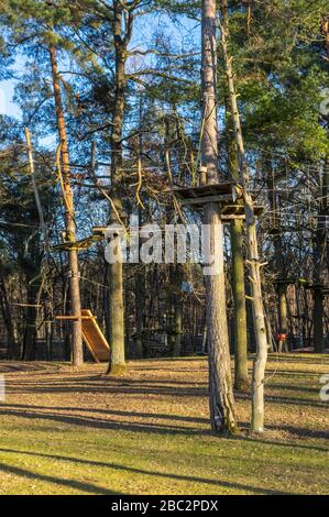 Giardino di arrampicata, alta corda corso nella foresta con vari elementi di arrampicata e corde di sicurezza tra i singoli alberi e panchine per riposare Foto Stock