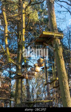 Giardino di arrampicata, alta corda corso nella foresta con vari elementi di arrampicata e corde di sicurezza tra i singoli alberi e panchine per riposare Foto Stock