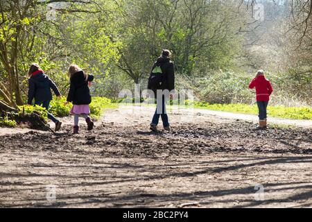 Madre & 3 bambini tre figlie bambini camminare / camminare lungo il sentiero fangoso / nel fango sul sentiero pedonale sentiero pedonale sentiero pedonale. West End Common, vicino a Esher, Surrey. REGNO UNITO (116) Foto Stock