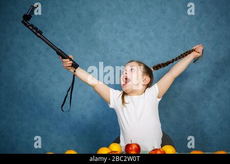 Bambina gioca con frutta e prende un selfie al telefono. Vitamine e nutrizione sana per i bambini. Foto Stock