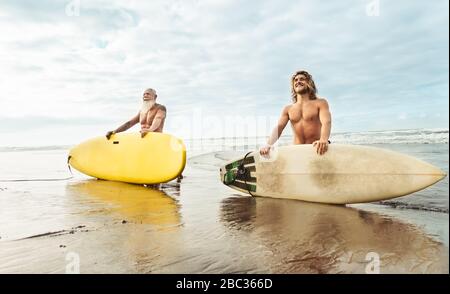 Montare felici amici divertendosi surf sul oceano tropicale - Surfers padre e figlio facendo stretching esercizi di surf Foto Stock