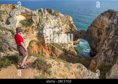 Donna in piedi sul bordo della scogliera vicino ad arco di mare, Pont Piedade, Algarve, Porgugal Foto Stock