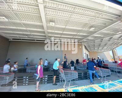 Gli acquirenti si allineano a Costco mantenendo le distanze sociali. Palette di legno sono state messe per aiutare la gente a tenere a parte e forma una linea con abbastanza spazio tra di loro. Foto Stock