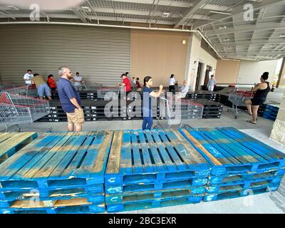 Gli acquirenti si allineano a Costco mantenendo le distanze sociali. Palette di legno sono state messe per aiutare la gente a tenere a parte e forma una linea con abbastanza spazio tra di loro. Foto Stock