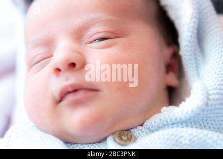 Primo piano ritratto di un neonato. Primo piano viso del neonato con occhi aperti. Un neonato sta guardando la lente da vicino. Neonato in blu Foto Stock