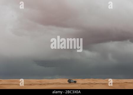 la jeep blu del bambino guida sulle dune di sabbia del deserto dello utah sotto i cieli stormi Foto Stock