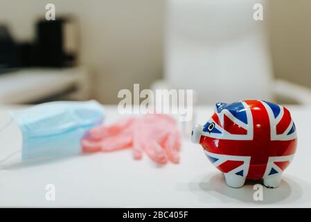 Una banca piggy con una bandiera inglese, guanti, maschera, una mela e un igienizzatore per le mani sul tavolo. COVID - 19 prevenzione Foto Stock