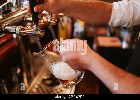 Un uomo in una caffetteria versa la birra dalla macchina. Alcol e un bicchiere Foto Stock