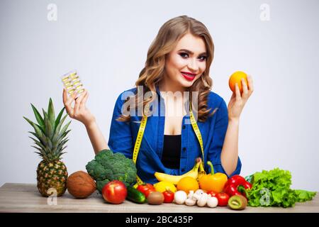 Donna a un tavolo che tiene un kiwi e pillole su uno sfondo di frutta e verdura Foto Stock