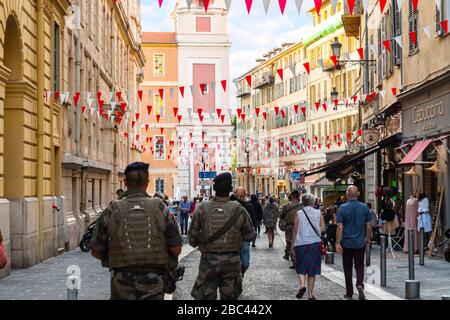Sicurezza militare polizia armata camminare attraverso la vecchia Vieux Nice, Francia, verso il Palazzo Rusca come bandiere drappeggiano attraverso il vicolo in ritardo nella giornata. Foto Stock