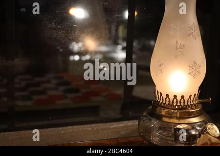 lampada hurricane con vetro smerigliato inciso con fiocchi di neve riflessi nella finestra di vetro Foto Stock