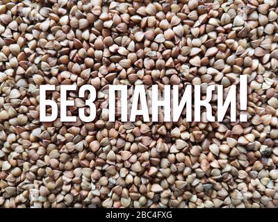 Fondo di grano saraceno sparso, piatto. Primo piano sullo sfondo di grano saraceno. Il testo 'Bez paniki' in lingua russa significa 'non panico'. Carenza di beni Foto Stock