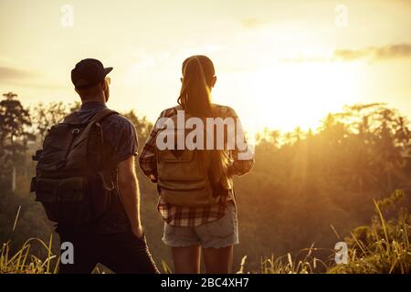 Un paio di viaggiatori si alza con zaini e guarda l'alba in tropici Foto Stock