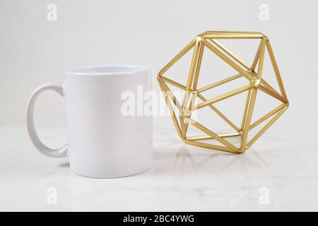 Una tazza di caffè da 11 once mockup con una moderna scultura astratta dorata che adorna lo sfondo. Foto Stock