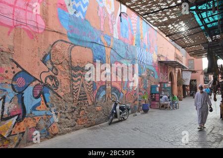 Arte di strada colorata e un uomo locale in abito tradizionale visto in un tour a piedi della medina di Marrakech, Marocco. Foto Stock