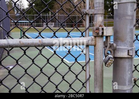 Il cancello di un campo da tennis è chiuso con una rete da tennis in background. Foto Stock