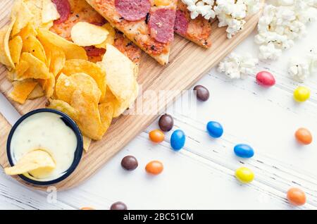 Fast food e malsano concetto di mangiare. Close up di un fast food snack: pizza, popcorn, patatine e caramelle. Assortimento di carboidrati prodotti ba Foto Stock