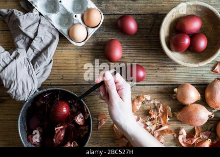 Donna che fa tinto uova di Pasqua dipinte con cipolla colorante naturale su sfondo di legno. Processo di tintura delle uova con vernici naturali per Pasqua. ecol naturale Foto Stock