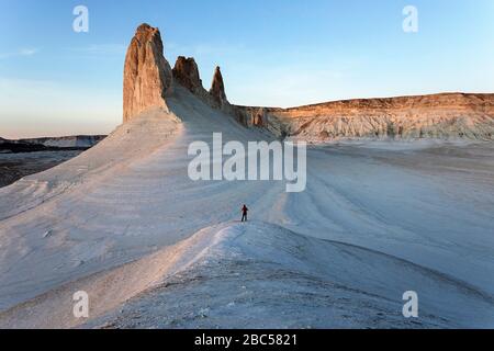 Donna in giacca rossa in piedi e guardando la vista sulle montagne calcaree, Ustyurt, Boszhira, deserto Caspio depressione, Aktau, Mangystau, Kazakhstan Foto Stock