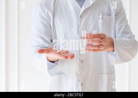 Il medico ha le mani che danno la capsula e un bicchiere d'acqua Foto Stock