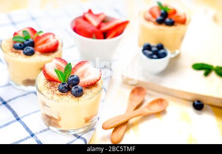 In casa, squisiti dessert Tiramisu' in vetri decorati con fragola, mirtillo, menta bianca sul tavolo di legno, Foto Stock