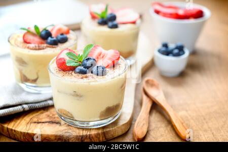 In casa, squisiti dessert Tiramisu' in vetri decorati con fragola, mirtillo, menta bianca sul tavolo di legno, Foto Stock