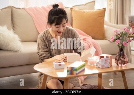 Giovane donna cinese che apre una confezione regalo a casa Foto Stock