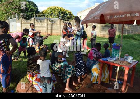 LILONGWE, MALAWI, AFRICA - 2 APRILE 2018: Strada luminosa, donne e bambini africani sono seduti lungo le strade, sorridendo e prendendo caramelle. Foto Stock