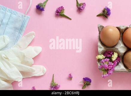 Guanti, maschera facciale, fiori e uova su sfondo rosa chiaro vista dall'alto. Pasqua durante il concetto di coronavirus. Foto Stock