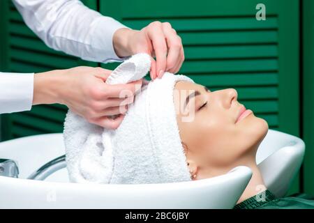 Parrucchiere che avvolge i capelli della donna in asciugamano dopo aver lavato la testa nel salone di bellezza, primo piano. Foto Stock