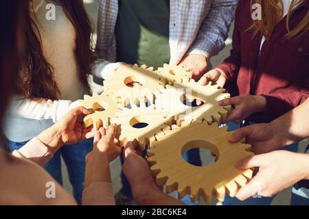 Un gruppo di giovani uomini d'affari in abiti casual stanno tenendo ingranaggi di legno con le loro mani. Foto Stock