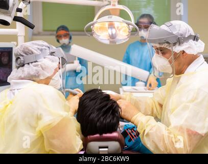 Dresda, Germania. 03rd Apr, 2020. ILLUSTRAZIONE - il dentista Conrad Kühnöl (r) tratta un paziente corona nella sua pratica dentale (scena posta) con visiera, maschera respiratoria FFP3 e abito antivirale insieme ai suoi assistenti dentali. Credito: Robert Michael/dpa-Zentralbild/dpa/Alamy Live News Foto Stock