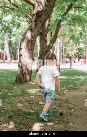 vista posteriore della bambina in maglietta vuota che cammina nel parco. Mockup per il design Foto Stock