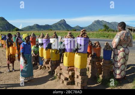 LILONGWE, MALAWI, AFRICA - 25 MARZO 2018: Quattro donne africane sorridono e vendono potatos lungo la strada per Dedza. Atmosfera felice, viola brillante Foto Stock