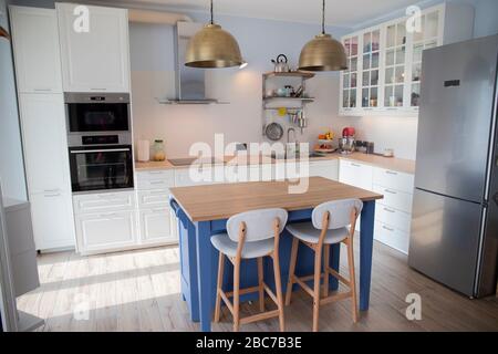 Cucina bianca e luminosa con isola blu e doppi lampadari in ottone. Foto Stock