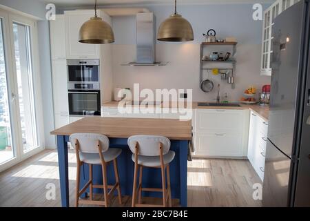 Cucina bianca e luminosa con isola blu e doppi lampadari in ottone. Foto Stock