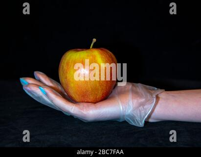 Una mela matura rossa è adagiata sulla mano di una donna in un guanto di gomma trasparente. Foto Stock