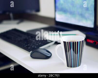 Scrivania da lavoro con computer portatile, tastiera, mouse, blocco note e tazza di caffè. Lavoro da casa filmato concettuale. Messa a fuoco in primo piano con una tazza di caffè Foto Stock