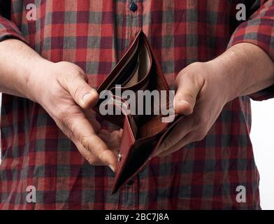 l'uomo in una camicia rossa a pacca tiene un portafoglio marrone in pelle vuoto, concetto di povertà e crisi economica Foto Stock