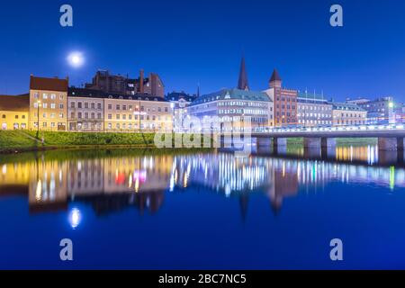 Città notturna specchiata nell'acqua. Panorama serale di una vecchia città europea. Paesaggio urbano di Malmo, Svezia Foto Stock