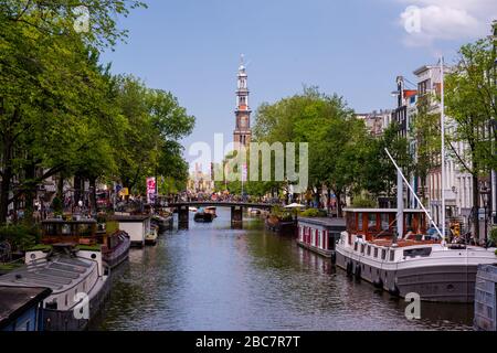 Amsterdam, Paesi Bassi -- 29 luglio 2019. Foto guardando lungo il canale Singel e passato un ponte che attraversa con la chiesa occidentale (Westerkerk) torre nel Foto Stock