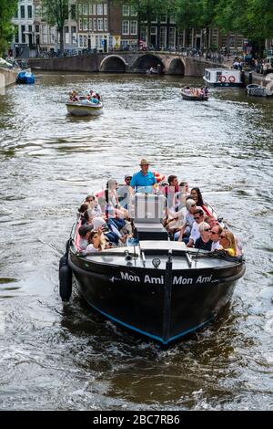 Amsterdam, Paesi Bassi -- 29 luglio 2019. Foto di un tour in barca pieno di persone che naviga in uno dei molti splendidi canali di Amsterdam in un pomeriggio estivo. Foto Stock